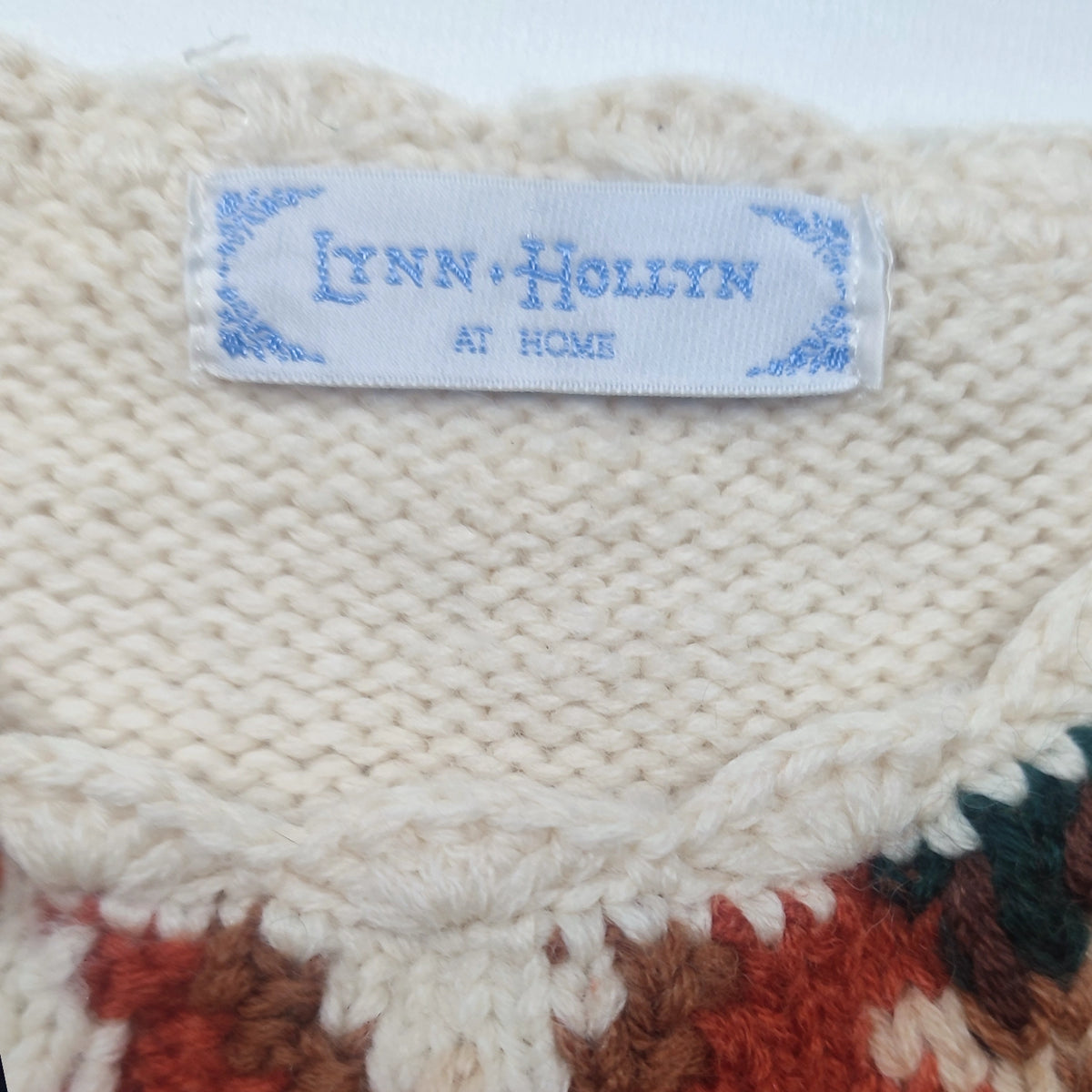 Lynn-Hollyn-at-Home-Etikett am cremefarbenen Strickkragen mit buntem Musteransatz.