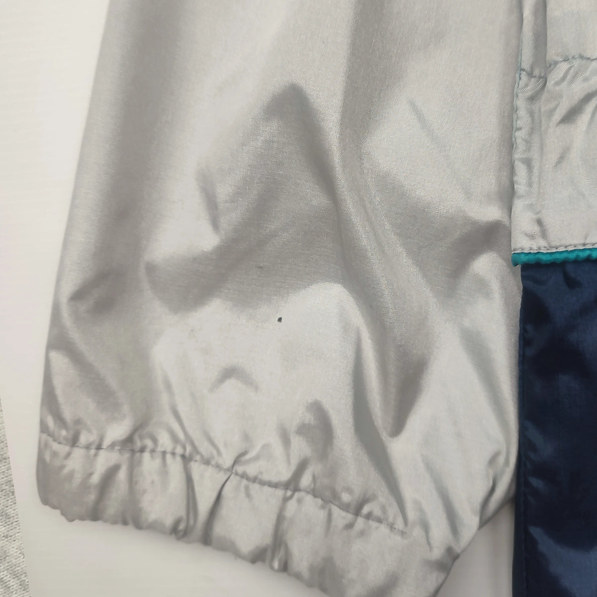 Langer Herosportif-Windbreaker in Grau und Marineblau mit türkiser Verschlussblende und Stehkragen – Detailansicht