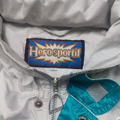Herosportif-Etikett mit Größe M im hellgrauen Kragen neben türkiser Blende, Reißverschluss und Druckknopf.
